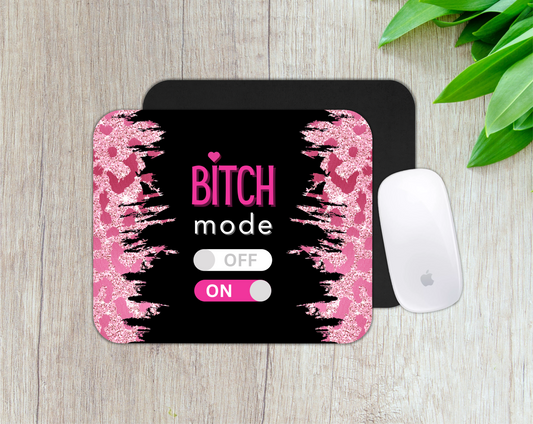 Mouse pad with 'Bitch mode' text on a wooden surface with a plant.